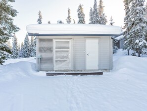 A small, single-story building with a snow-covered roof, a door, and a window with horizontal blinds.