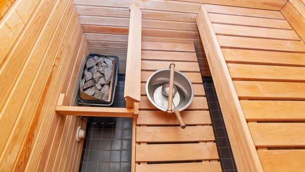 A sauna with wooden benches, a metal basin, and a tray of stones.