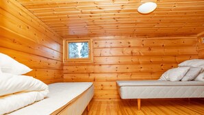 A cabin with wooden walls and floors, a window with a view of trees, two beds with white bedding, and a ceiling light.