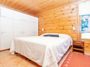 A bedroom with a wooden ceiling, a bed with a white bedspread, a nightstand, and a window with a view of snow-covered trees. - Rukan nietosrinne by Interhome (Kuusamo)