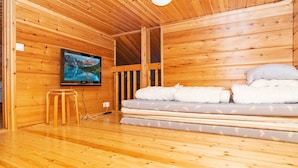 A wooden cabin interior with a bed, a television, and a wooden floor.