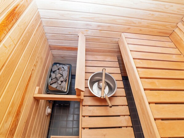 A sauna with wooden benches, a metal basin, and a tray of stones.