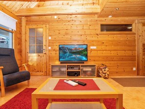 A wooden interior with a television on a stand, a chair, and a table with a remote control.