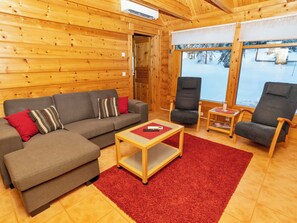 A cozy room with a wooden interior, a sofa, two chairs, a small table, and a window with a snowy view. - Rukan nietosrinne by Interhome (Kuusamo)
