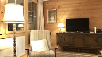 Ein gemütliches Wohnzimmer mit holzverkleideter Wand, einem Fernseher, einem Schrank und einem gemusterten Sessel.