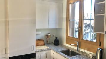 Eine moderne Küche mit weißen Schränken, einer Granit-Arbeitsplatte, einem Edelstahl-Spülbecken und einem Fenster mit Blick ins Freie.
