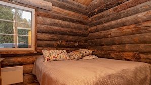 Ein Schlafzimmer in einer Blockhütte mit einem Bett, Kissen, einem Fenster und einem Heizgerät.
