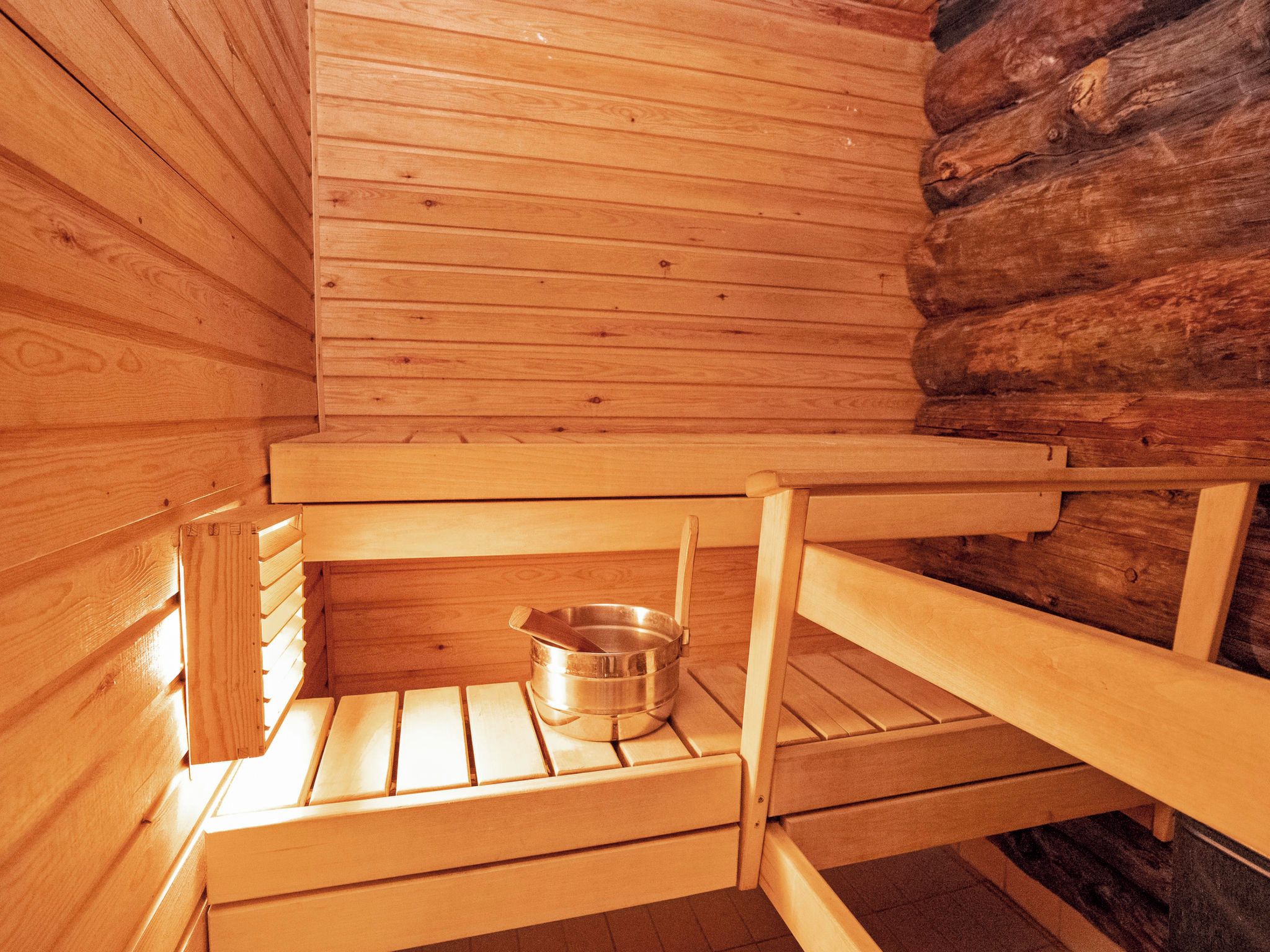 A wooden sauna with benches and a metal basin.