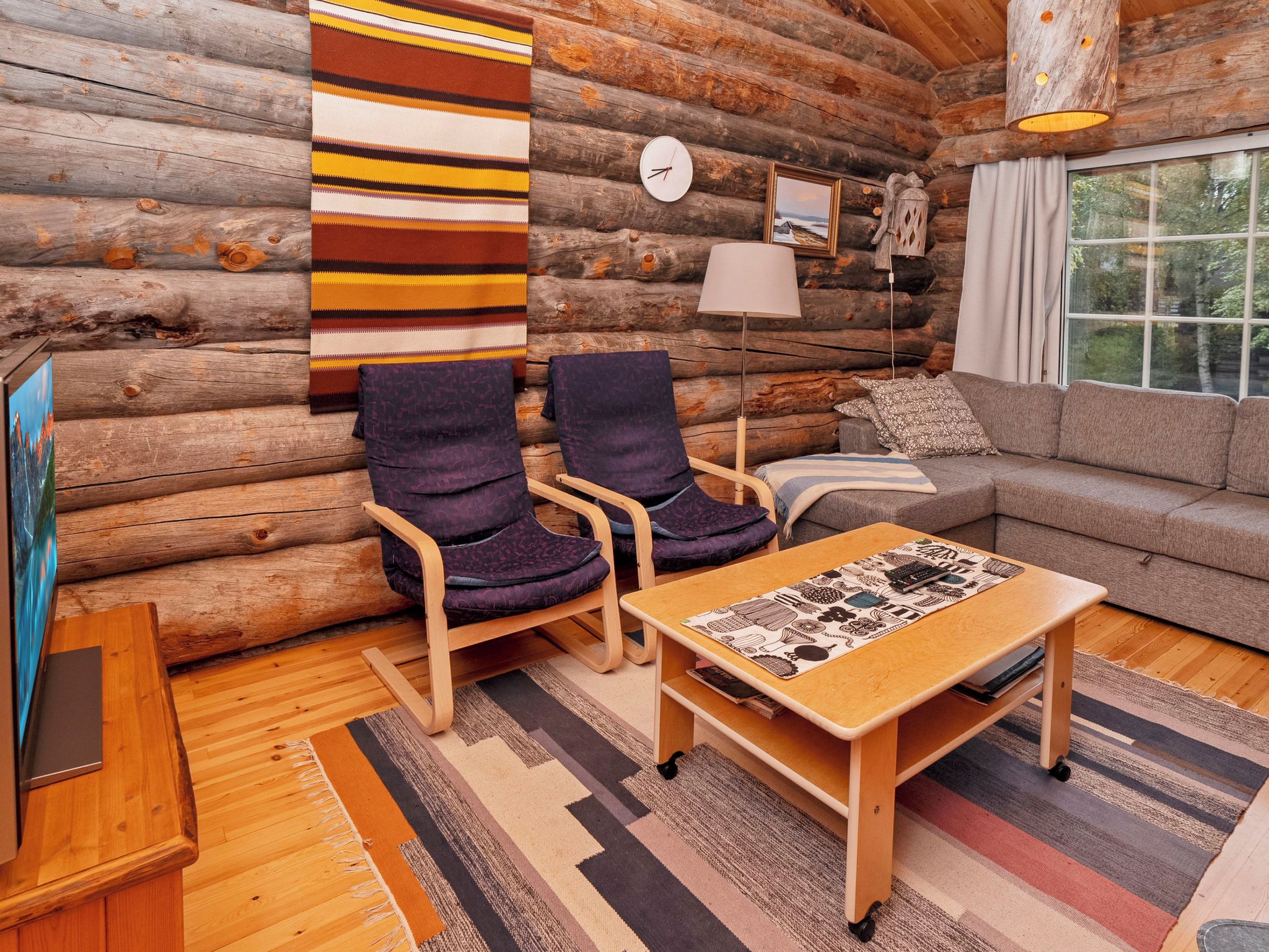 A log cabin interior with a sofa, two armchairs, a coffee table, a clock, and a lamp.