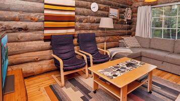 A log cabin interior with a sofa, two armchairs, a coffee table, a clock, and a lamp.