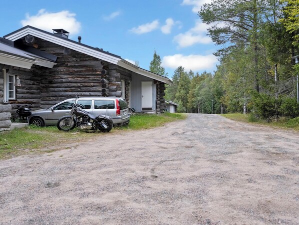 A log cabin with a gravel driveway, a parked car, and a motorcycle.