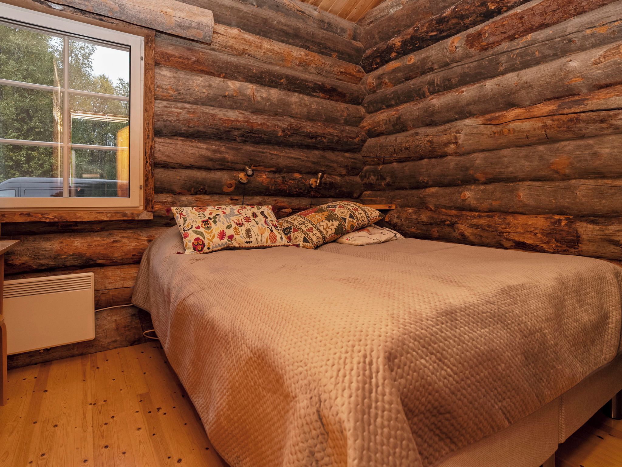 A log cabin bedroom with a bed, pillows, a heater, and a window.