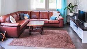 Un salon avec un canapé d’angle en cuir marron, une table basse en bois, un meuble pour la télévision avec un écran plat, et une plante en pot.