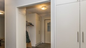 Un couloir avec des armoires blanches, un porte-manteau et une porte donnant sur une autre pièce.