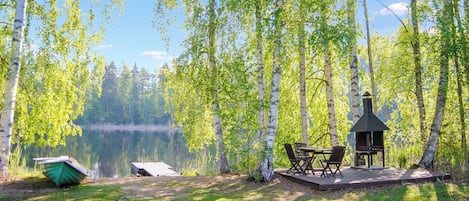 A lakeside outdoor area with a deck, a grill, and a boat.