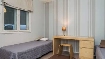 Een slaapkamer met twee enkele bedden, een bureau met stoel, een raam met gordijnen en een wandlamp.
