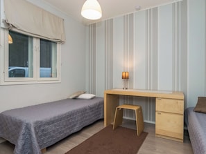 Une chambre avec deux lits simples, un bureau avec une chaise, une fenêtre avec des rideaux et une lampe fixée au mur.