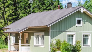 Une maison verte avec un porche, une cheminée et une petite fenêtre.