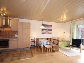 Eine gemütliche Küche mit Holzausbau, einem Esstisch mit Stühlen, einer Couch und einem großen Fenster mit Vorhängen.