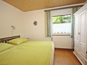Ein Schlafzimmer mit zwei Betten, einem Heizkörper, einem Fenster mit Vorhängen und einem Kleiderschrank.