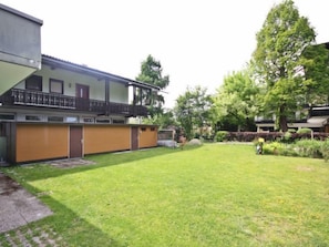 Ein Gebäude mit flachem Dach, einem Balkon und einem eingezäunten Garten mit Gras und Bäumen.