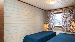 A room with two single beds, wooden flooring, a window with patterned curtains, and a ceiling light.