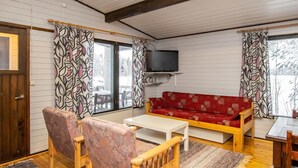 A cozy living room with a red sofa, wooden chairs, a white coffee table, and a television mounted on the wall.