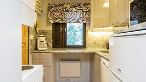 A compact kitchen with wooden cabinets, a built-in stove, a coffee maker, and a window with a view of trees.