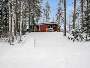 A cabin with a red exterior, surrounded by snow-covered trees.