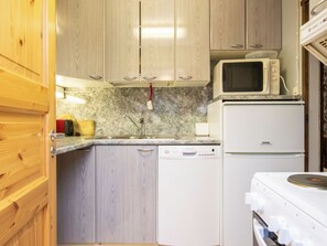 Een compacte keuken met houten kastjes, een magnetron, een vaatwasser en een fornuis.