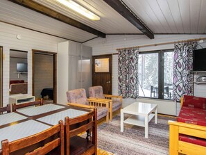 Una habitación acogedora con techo de madera, una mesa de comedor con sillas, un sofá, un televisor y una ventana con cortinas estampadas.