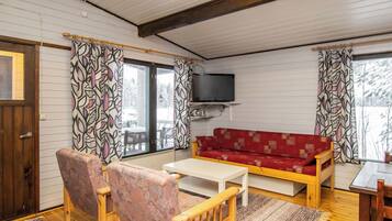 Una sala de estar acogedora con un sofá rojo, sillas de madera, un televisor y una ventana con cortinas estampadas.