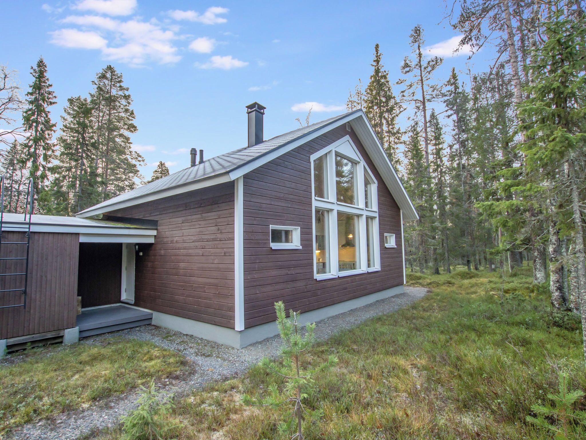 Puinen mökki, jossa on suuri ikkuna ja savupiippu, ja sen ympärillä on metsää.