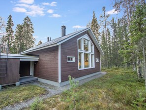 Une cabane en bois dotée d’une grande fenêtre et d’une cheminée, entourée d’une forêt.