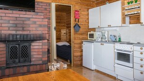 A compact kitchen with a brick fireplace, white cabinets, a microwave, and a stove. - Eteläranta by Interhome (Joutsa)