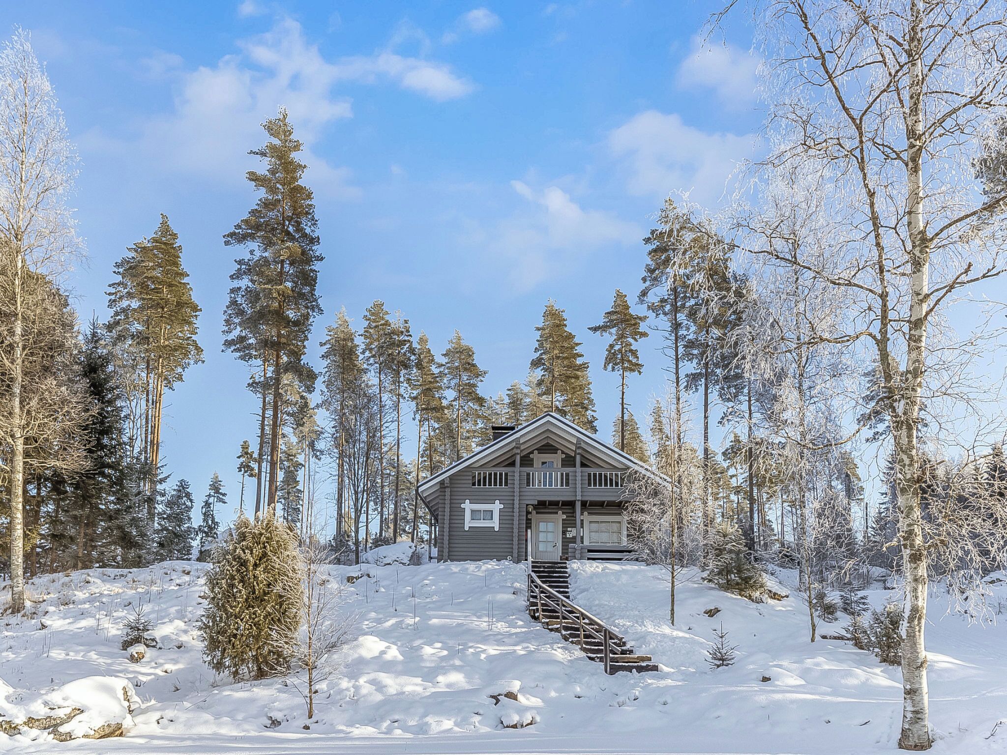 Eine Holzhütte, umgeben von hoch aufragenden immergrünen Bäumen, in einer verschneiten Landschaft.