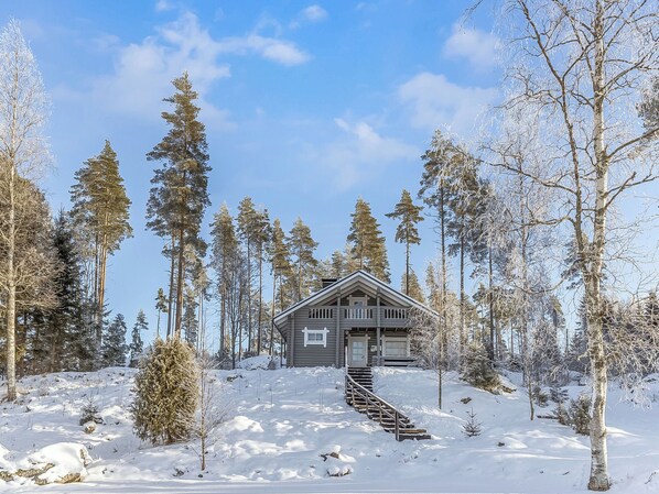 A cabin with a wooden exterior, surrounded by tall evergreen trees, in a snowy landscape. - Eteläranta by Interhome (Joutsa)
