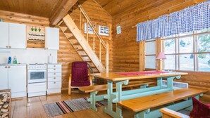 A cozy cabin interior with a wooden staircase, a kitchen area, a dining table, and a window with a view of trees. - Eteläranta by Interhome (Joutsa)