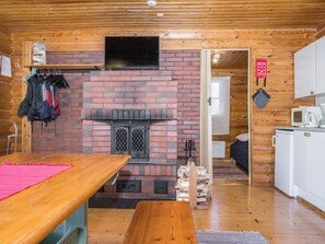 A cozy cabin with a brick fireplace, wooden walls, a dining area, and a kitchenette. - Eteläranta by Interhome (Joutsa)