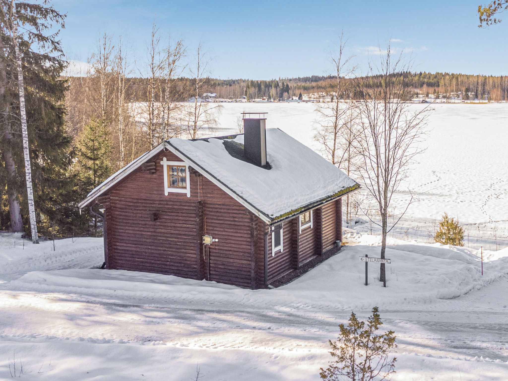 Eine Holzhütte mit einem mit Schnee bedeckten Dach, umgeben von verschneiter Landschaft und Bäumen.