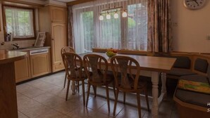 A kitchen with wooden cabinets, a dining table with chairs, a clock on the wall, and a window with curtains. - Bergfink by Interhome (Saas-Fee)