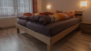 A double bed with a wooden frame, two bedside tables, and a window with sheer curtains. - Bergfink by Interhome (Saas-Fee)