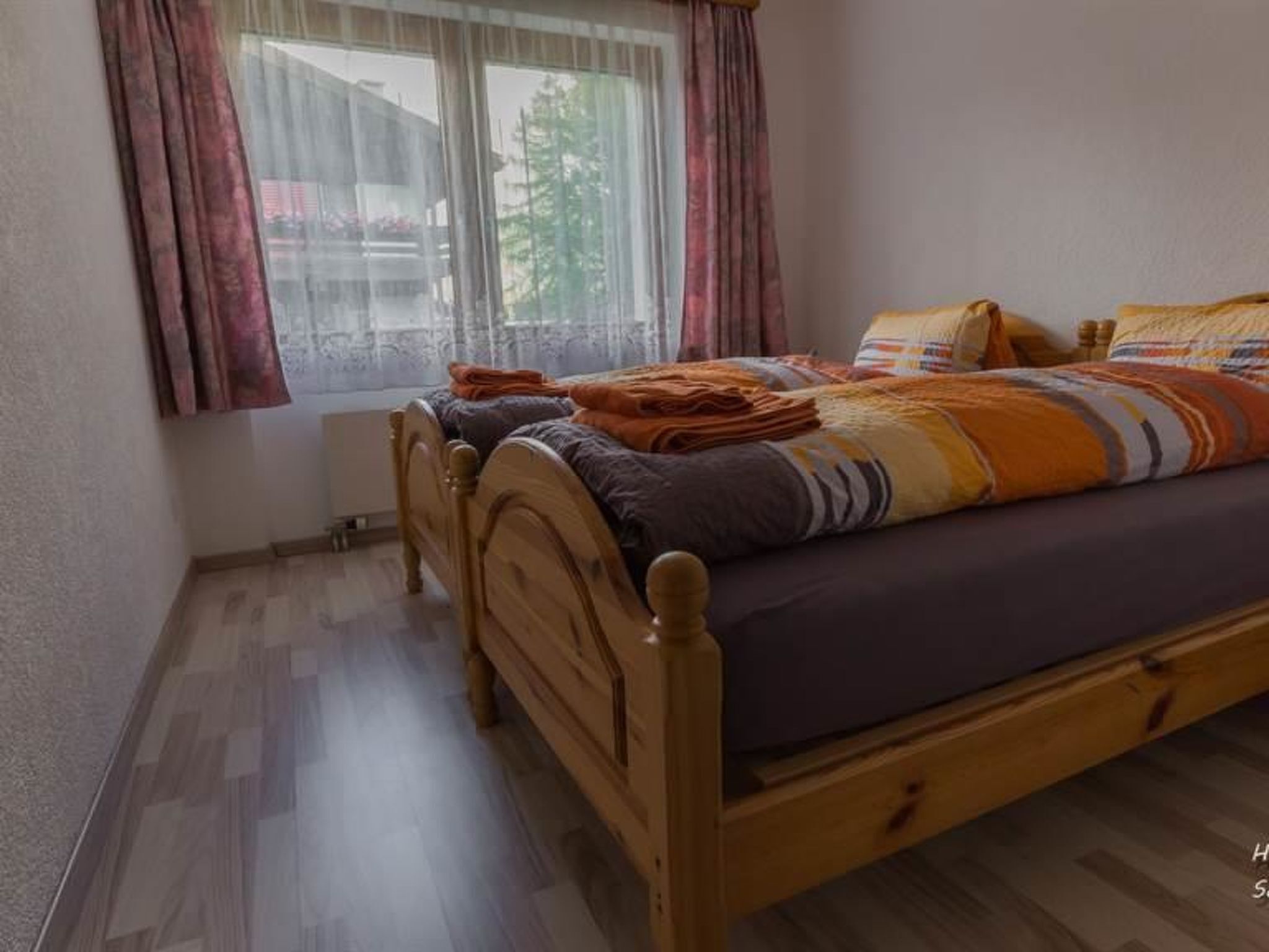 A bedroom with a wooden bed, a window with curtains, and a radiator.