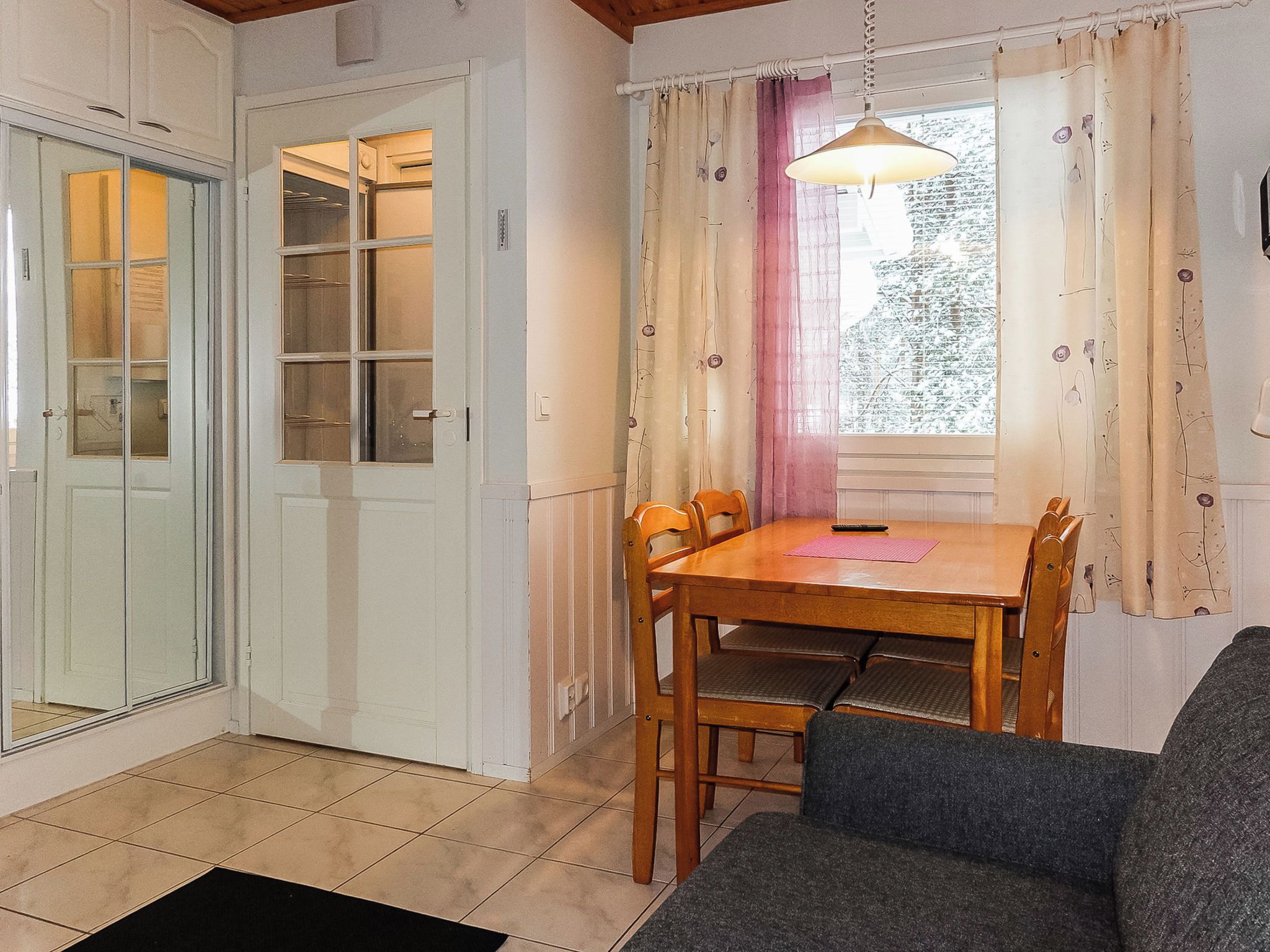 A room with a dining table, chairs, a sofa, a window with curtains, and a door with a glass panel.