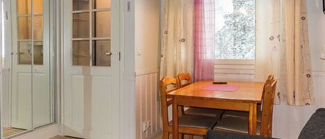 A room with a dining table, chairs, a sofa, a window with curtains, and a door with a glass panel.