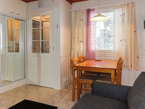 A room with a dining table, chairs, a sofa, a window with curtains, and a door with a glass panel.