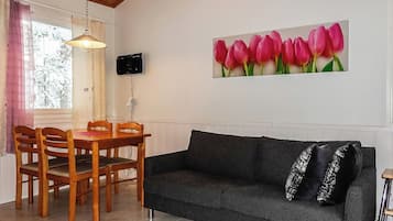 Sala de estar com mesa de jantar, cadeiras, sofá, televisão fixada na parede e janela com cortinas.