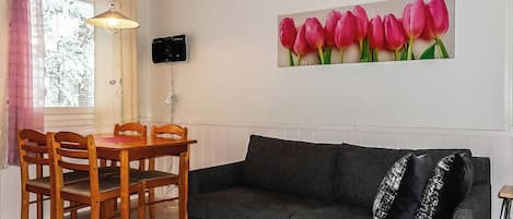 A living room with a dining table, chairs, a sofa, a TV mounted on the wall, and a window with curtains.