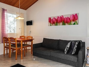 A living room with a dining table, chairs, a sofa, a TV mounted on the wall, and a window with curtains.