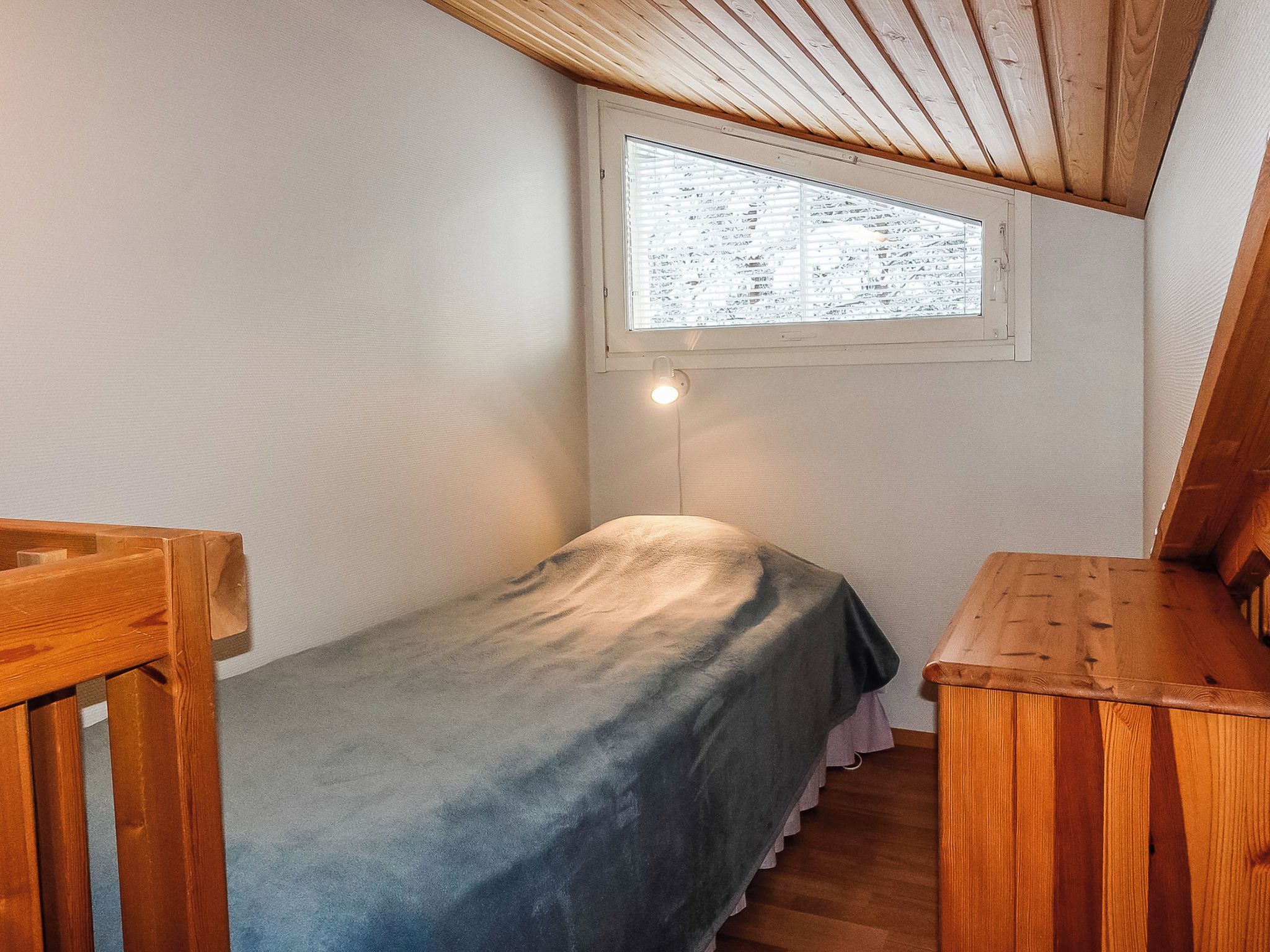 A small, single-bed room with a sloped ceiling and a window.